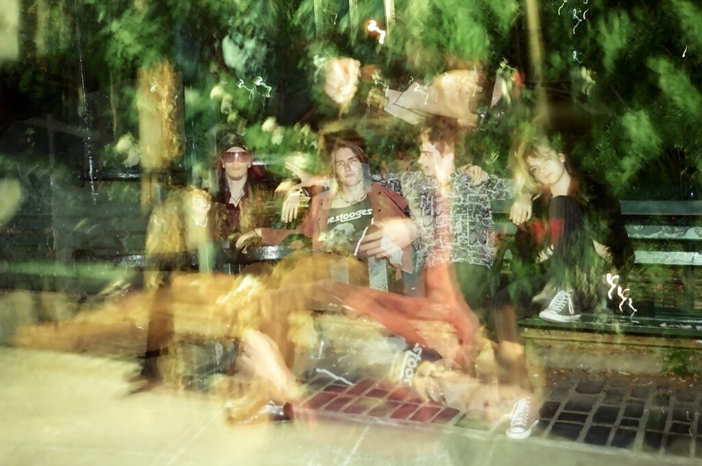 The members of nonequator sitting on a park bench in a hazy landscape. Left to right: Mitch Owens, Owen Pattillo, Carter Nyhan, Ayla Huguenot